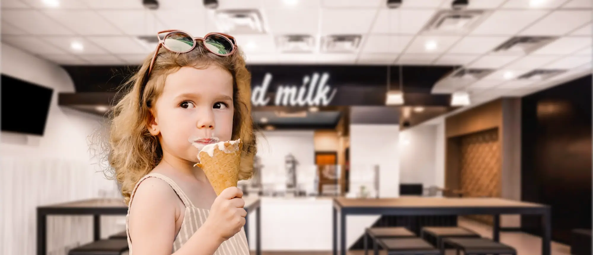 A young girl licking an ice cream cone that has almost been finished inside of a spilled milk store